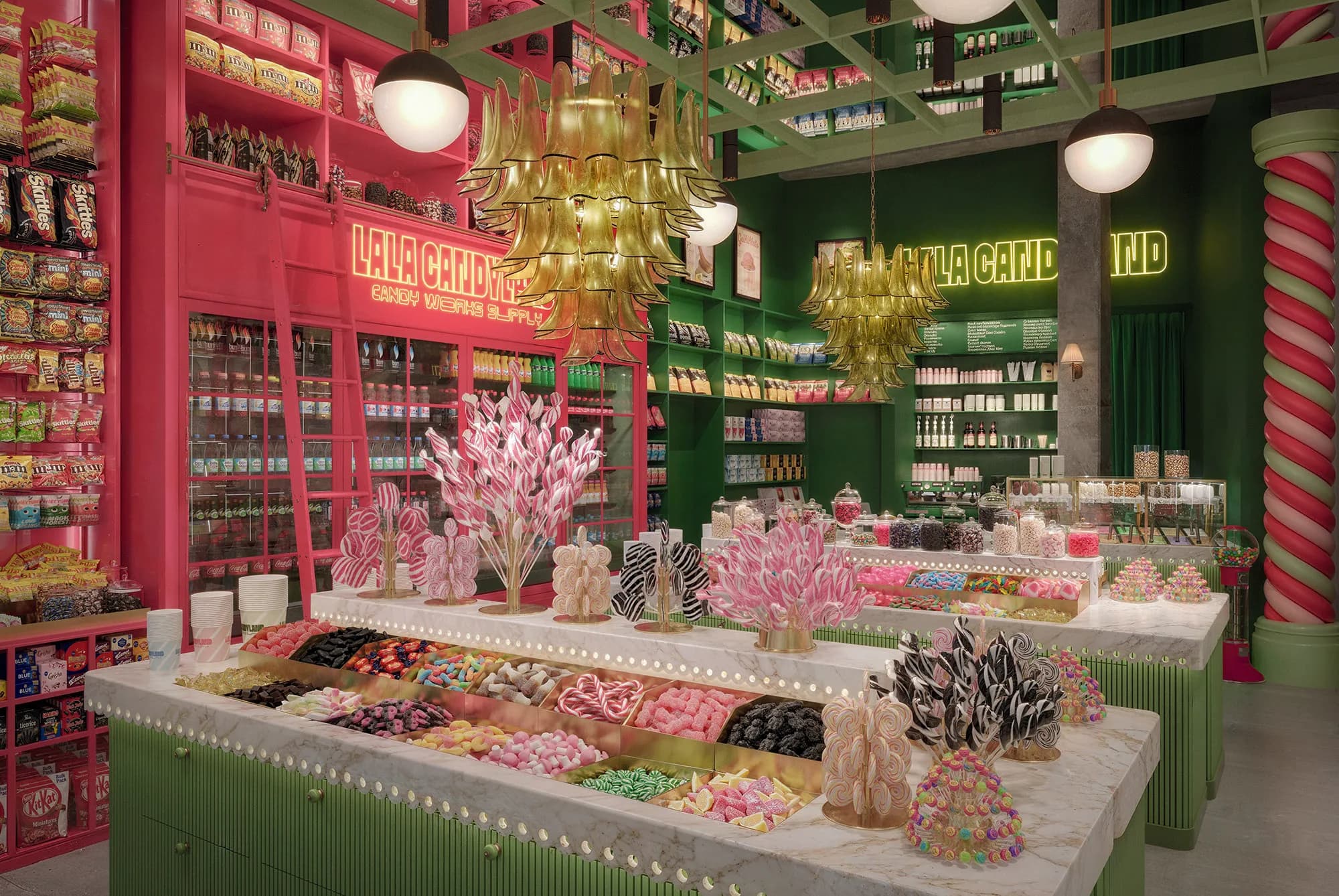 A white marble pick-and-mix counter edged with glowing bulbs, its brass bins full of gummies, sour sweets and liquorice, with pink and black swirl lollipop trees on top and a raspberry wall of shelves and a rolling ladder behind.